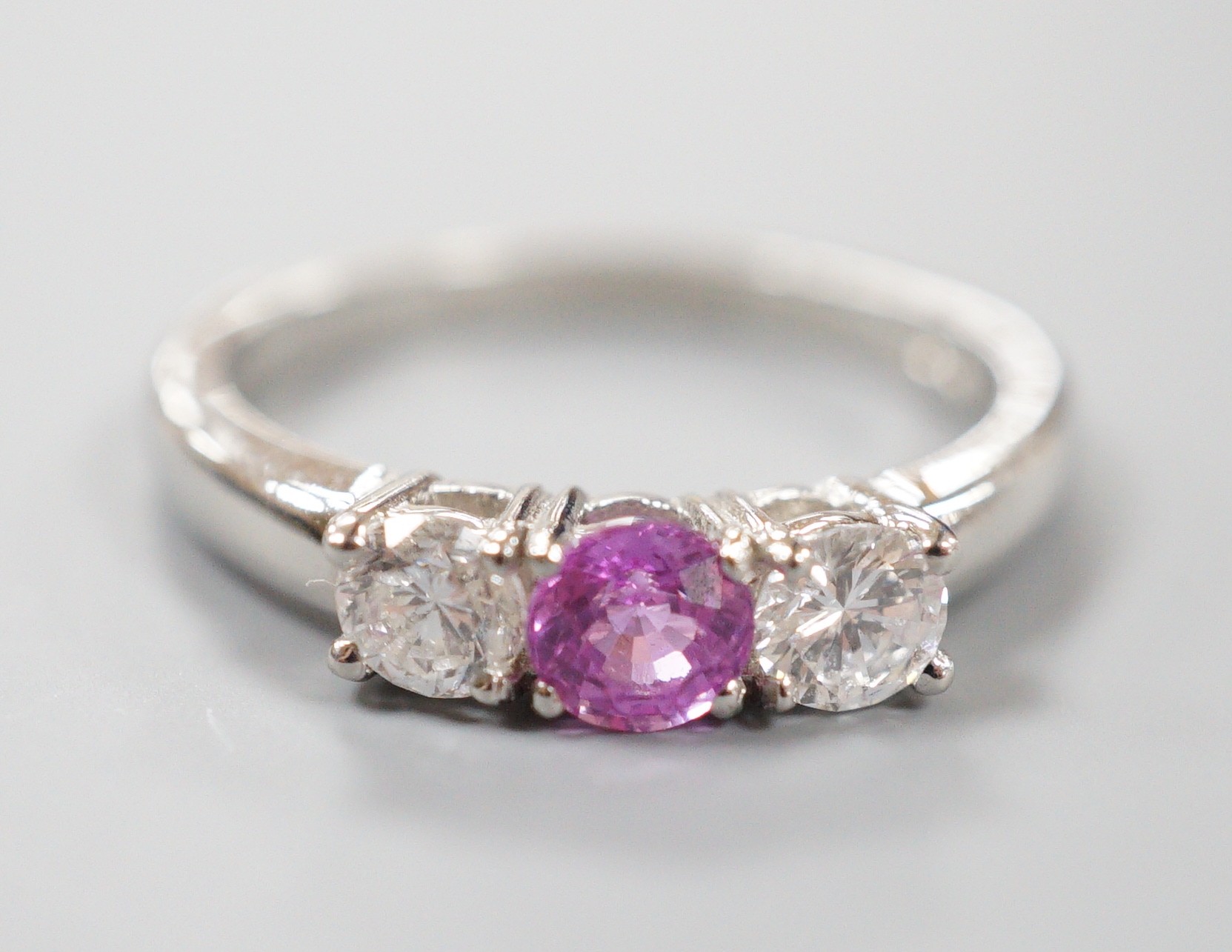 A modern platinum, pink sapphire and two stone round cut diamond set ring, size O, gross weight 5.4 grams